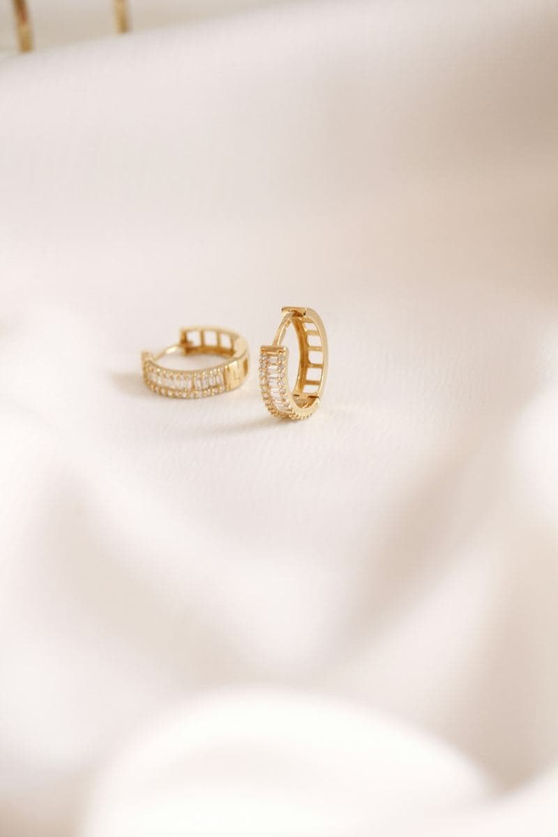 Pair of huggies with a center row of baguettes framed by round stones, open ladder-style backs, yellow gold