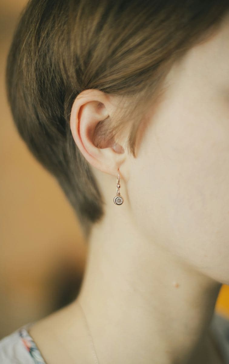 Earlobe wearing a small bezel-set round stone hanging from a rose-gold French wire