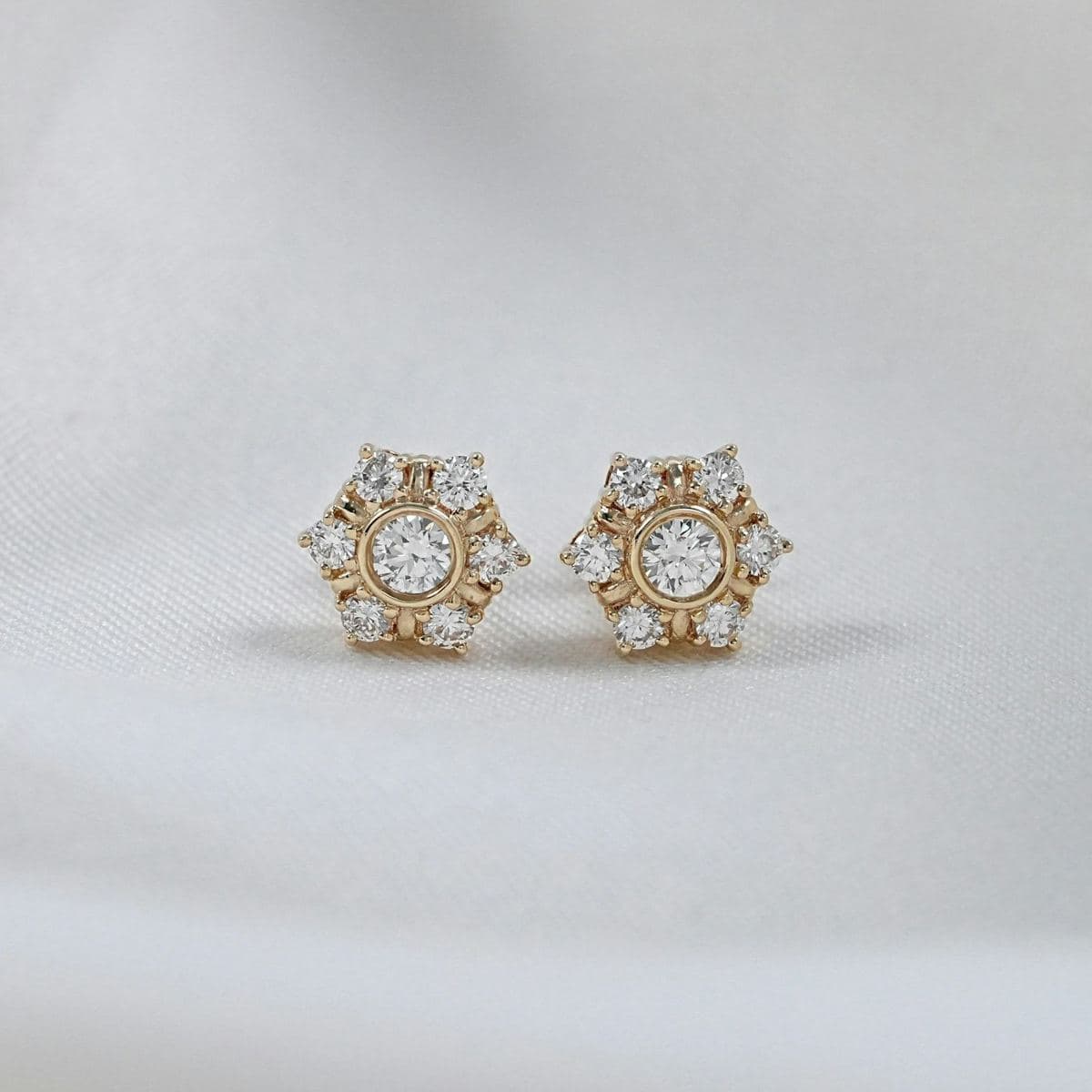 Pair of hexagon cluster studs: bezel-set round center with six prong-set round stones around it, yellow gold