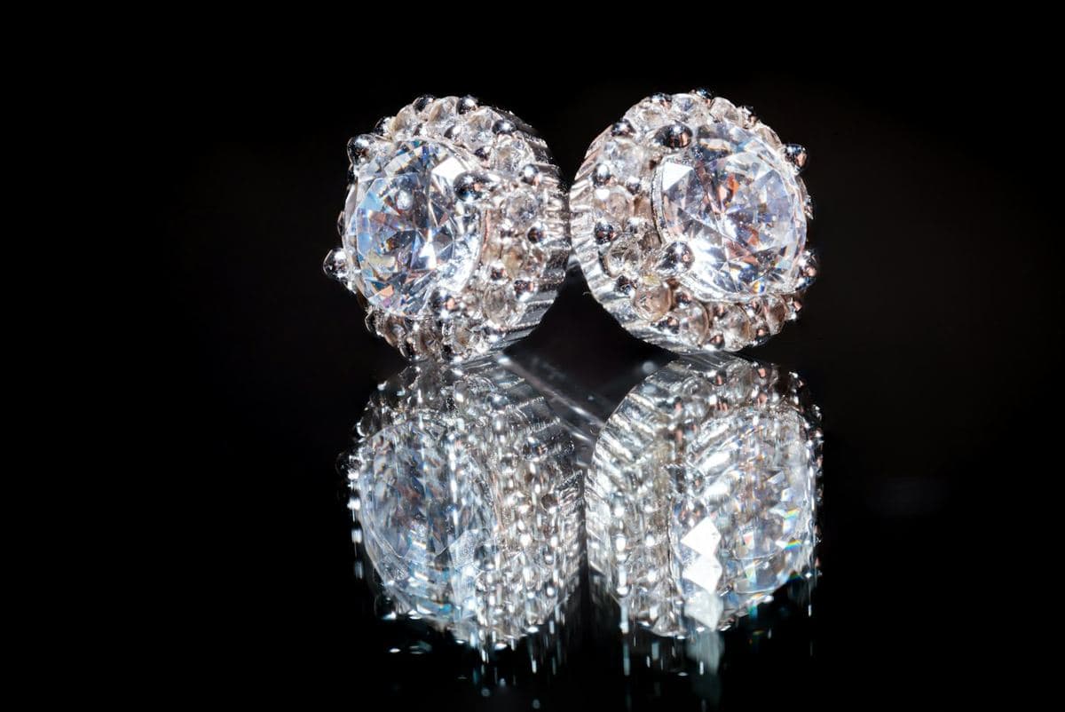 Pair of large round center stones with a halo of smaller round stones in white metal, mirrored on glossy black