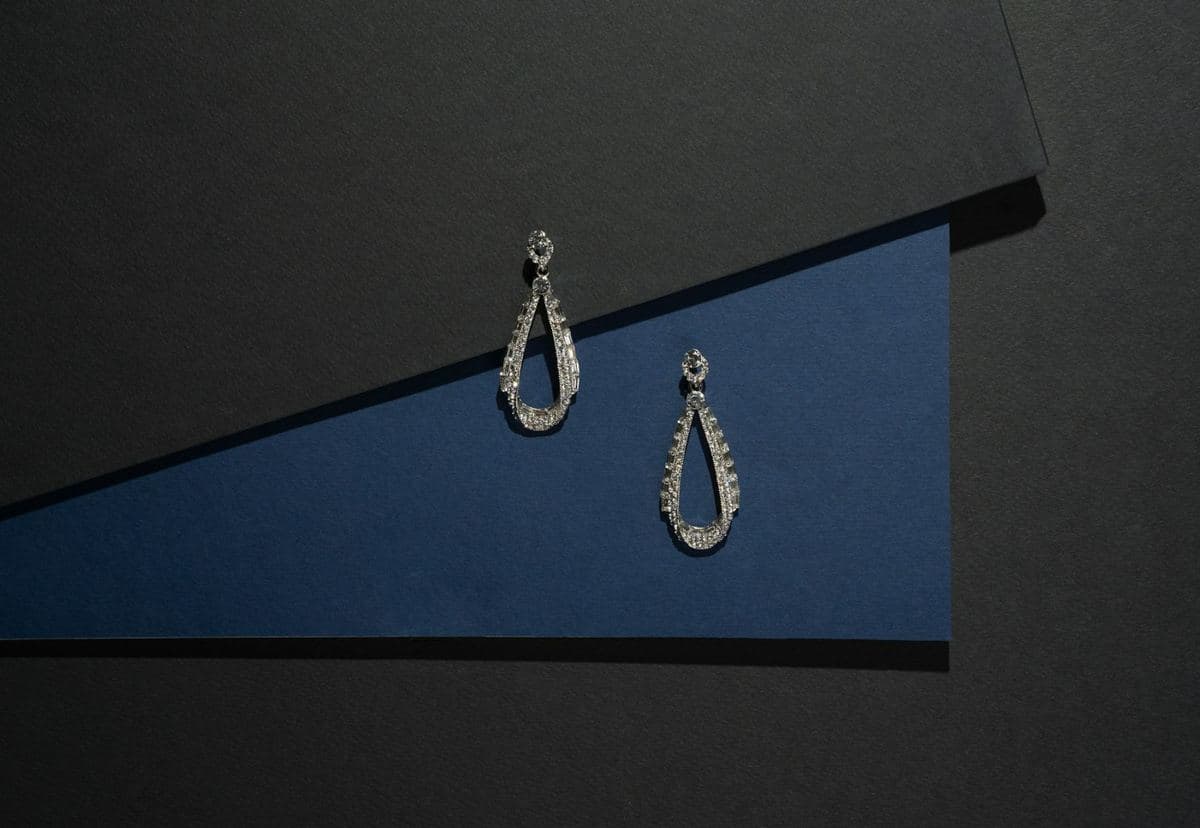Pair of open teardrop drops lined with baguette and round stones hanging from small round-stone tops, white metal