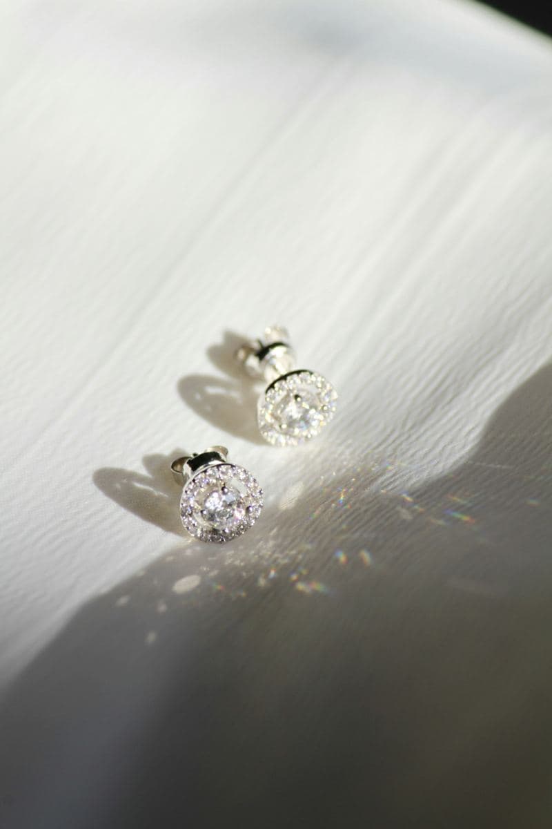 Pair of round center-stone studs each in a halo of small round stones, white metal with butterfly backs