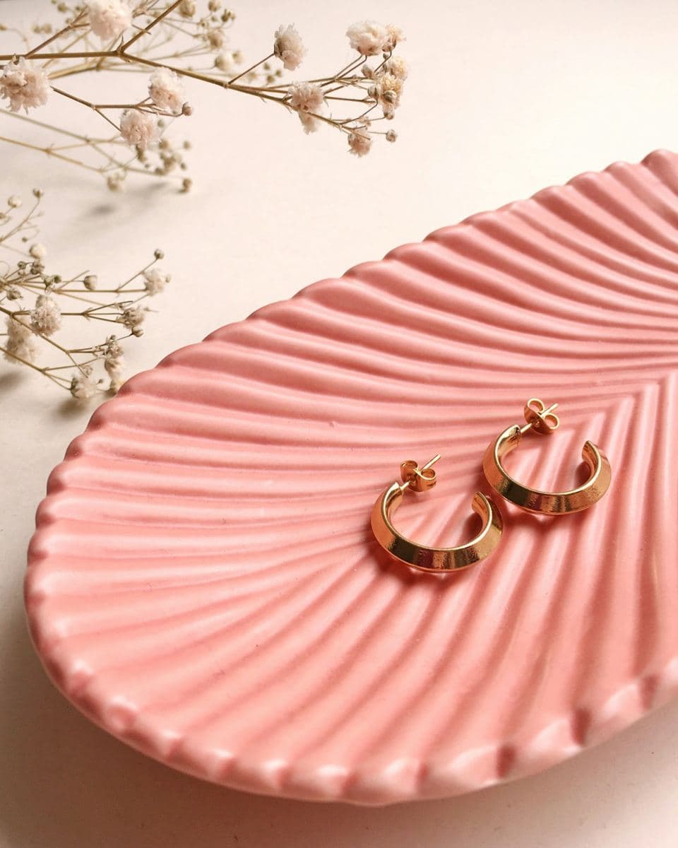 Pair of thick polished yellow-gold open half-hoops with post backs on a pink ceramic dish