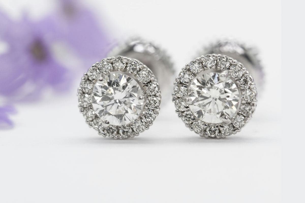 Pair of round prong-set center stones each ringed by a halo of small round stones in white metal, screw backs visible behind