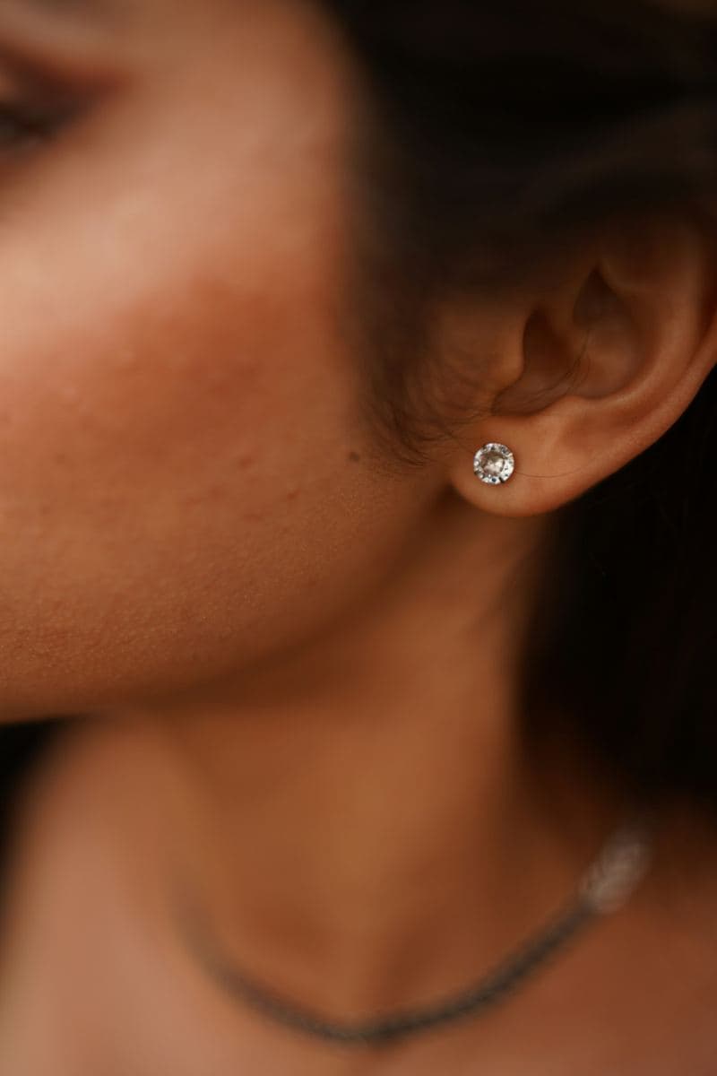 Close-up of an earlobe wearing a single round solitaire stud in a white-metal setting