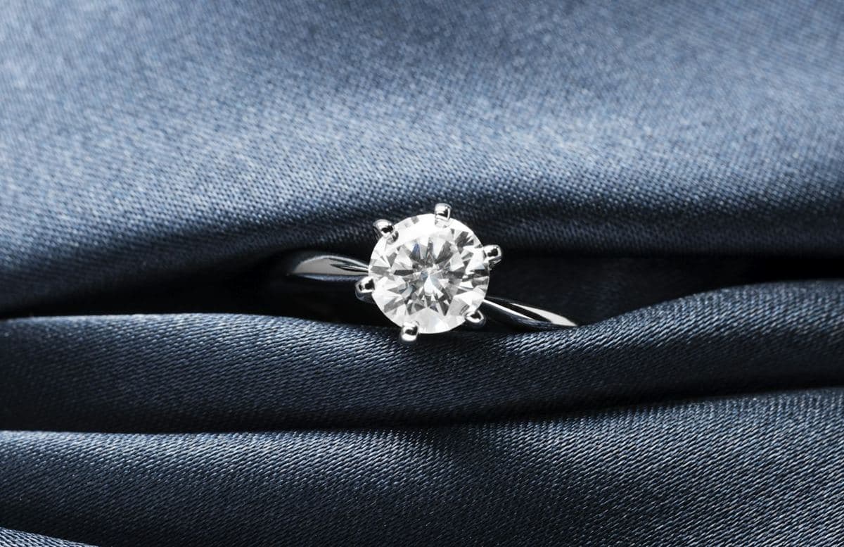 Round brilliant held in six prongs on a plain white-gold band, tucked into folded navy satin