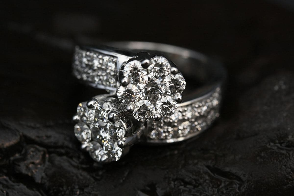 Bypass ring with two round-stone flower clusters on wide pavé white-metal shoulders