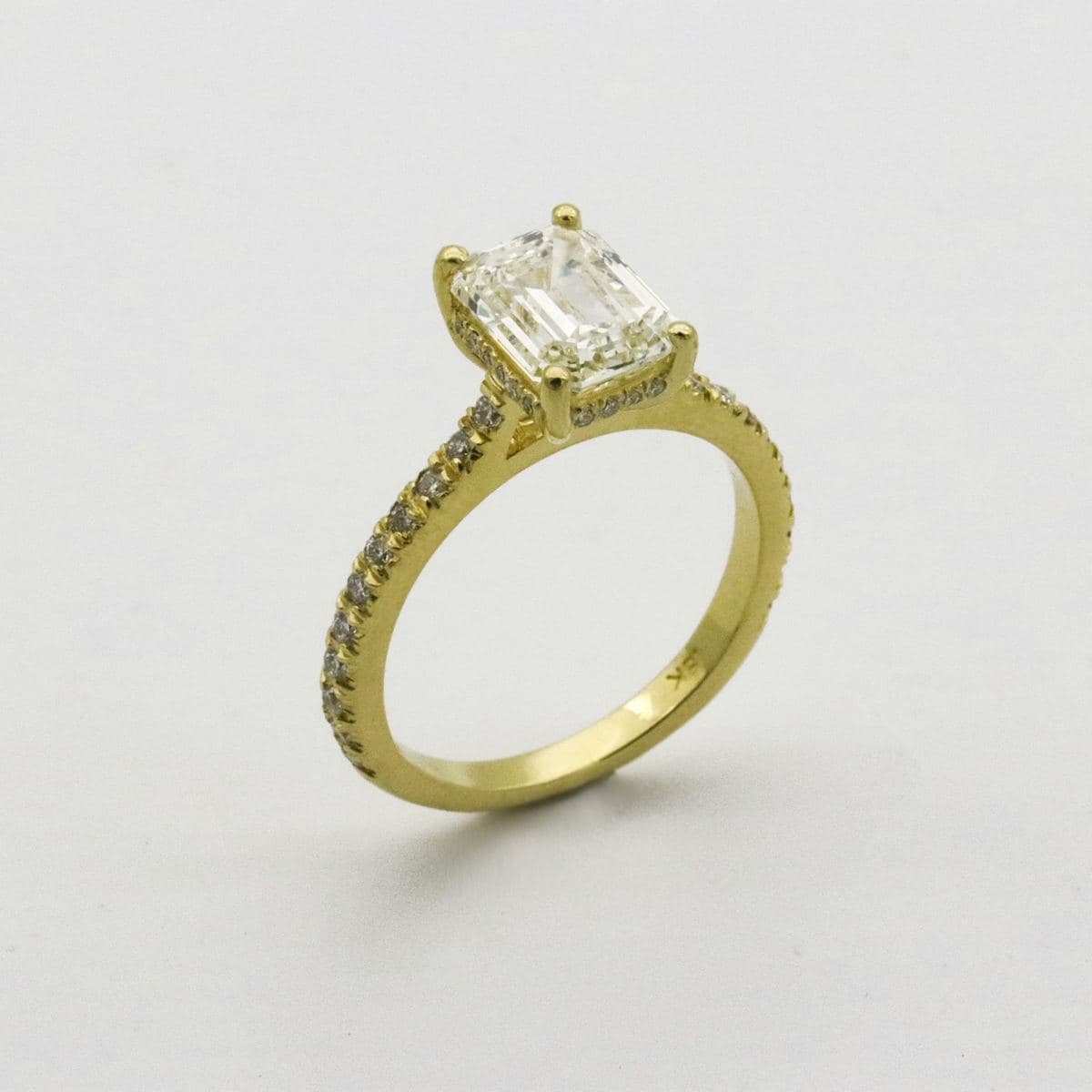 Emerald-cut center in four prongs with a pavé hidden halo and pavé shank, all yellow gold