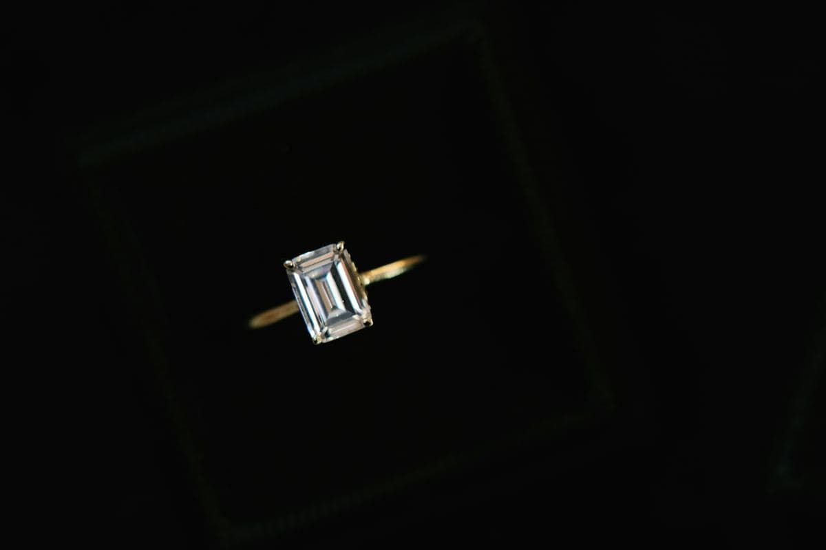 Emerald-cut center in four prongs on a very thin plain yellow-gold band, top-down in a dark box