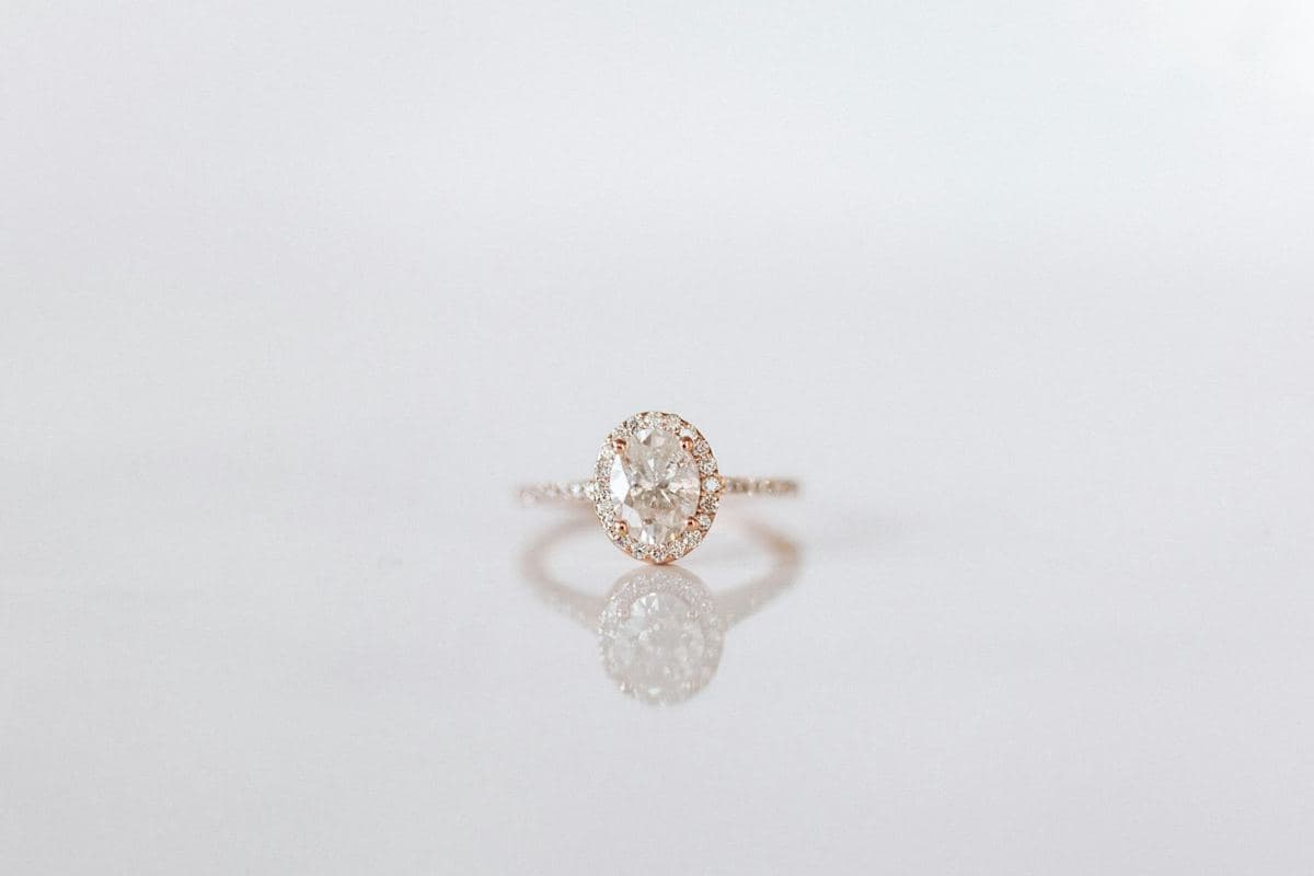 Oval center in a pavé halo on a rose-gold pavé band, small in frame with mirror reflection