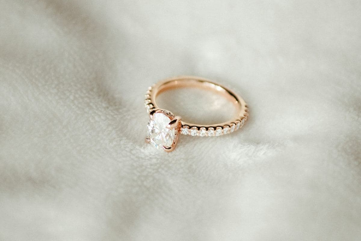 Oval center in four claw prongs on a rose-gold band with pavé stones across the shank