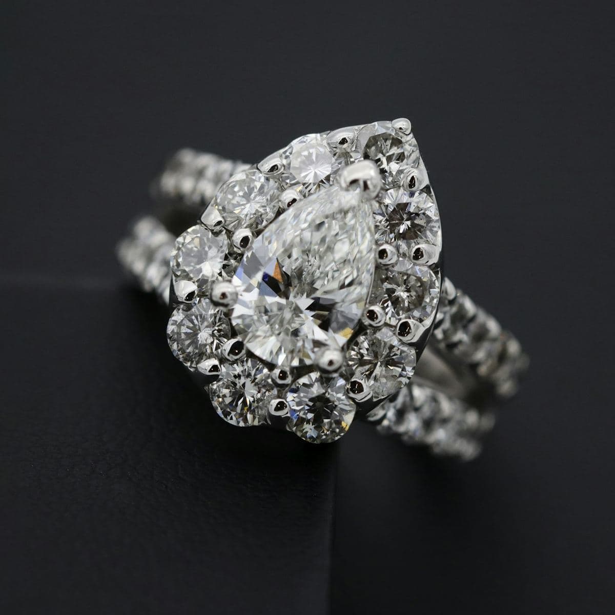 Pear center ringed by a halo of large prong-set round stones, with stone bands behind