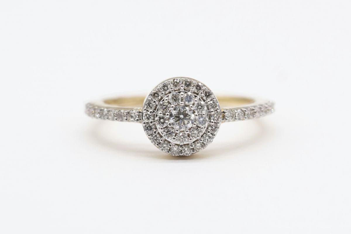 Small round center surrounded by a cluster and halo in white metal on a yellow-gold pavé band