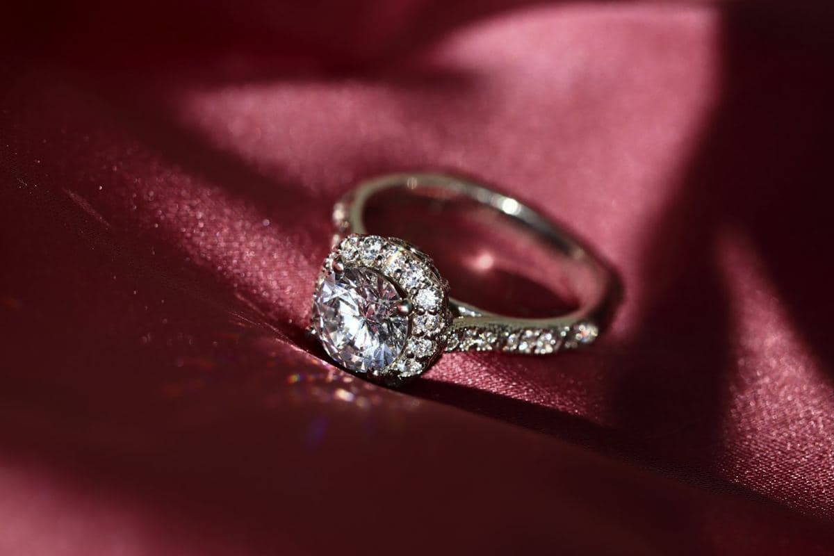 Round center inside a cushion-shaped stone halo on a white-gold pavé band