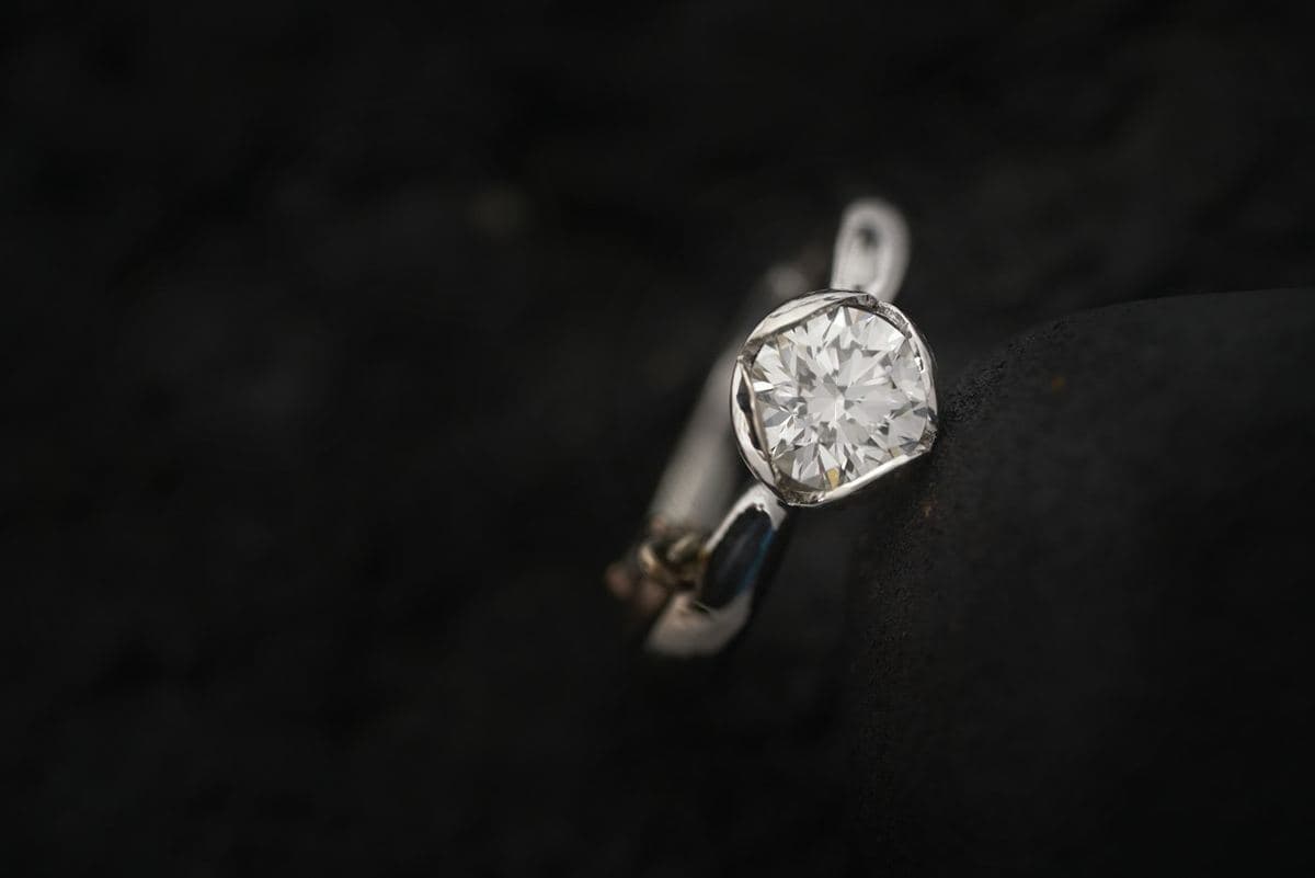 Round brilliant in a sculpted open half-bezel on a high-polish white-metal band, low-key lighting