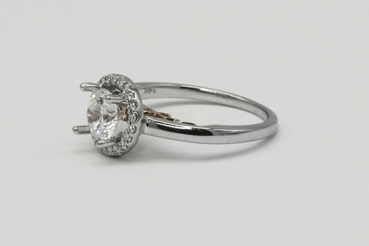 Side view of a round center in a pavé halo on a polished white-gold band with rose-gold gallery detail