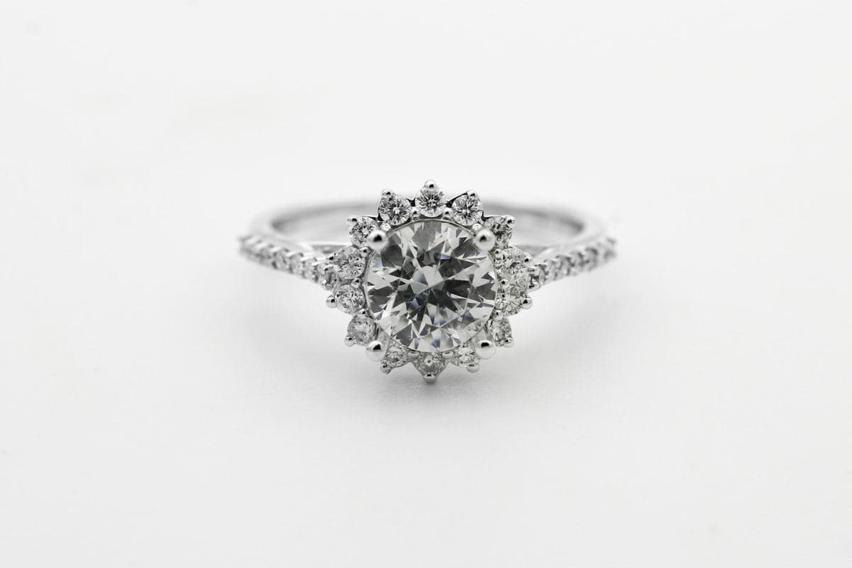 Round center surrounded by a scalloped sunburst halo of round stones on a pavé white-gold band