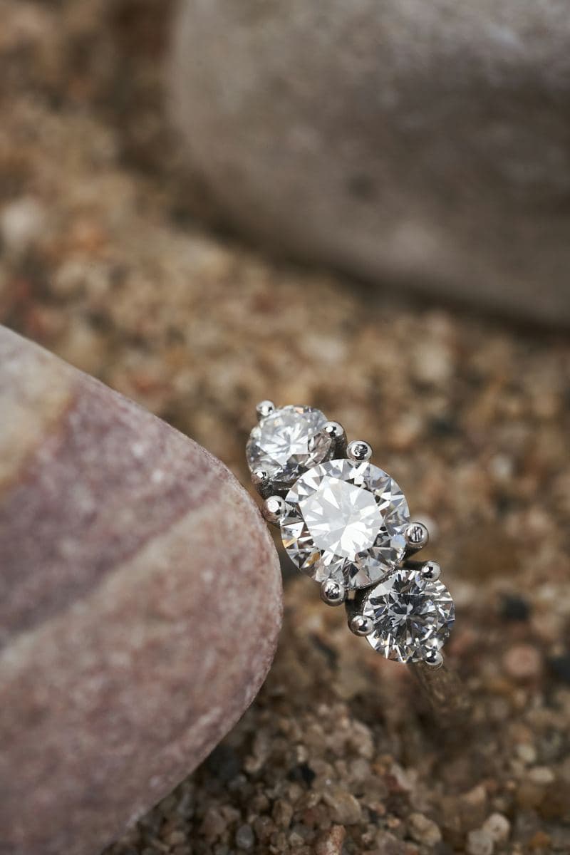 Three round brilliants in prong settings, larger center, on a white-metal band, close macro