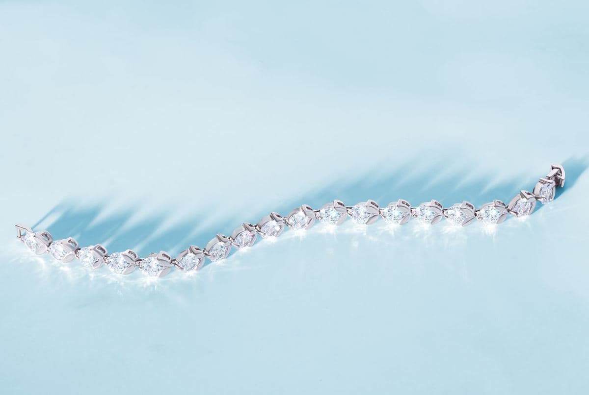 A straight line of about 19 uniform pear-shaped white stones in white-metal settings with a box clasp at one end, laid flat on pale blue