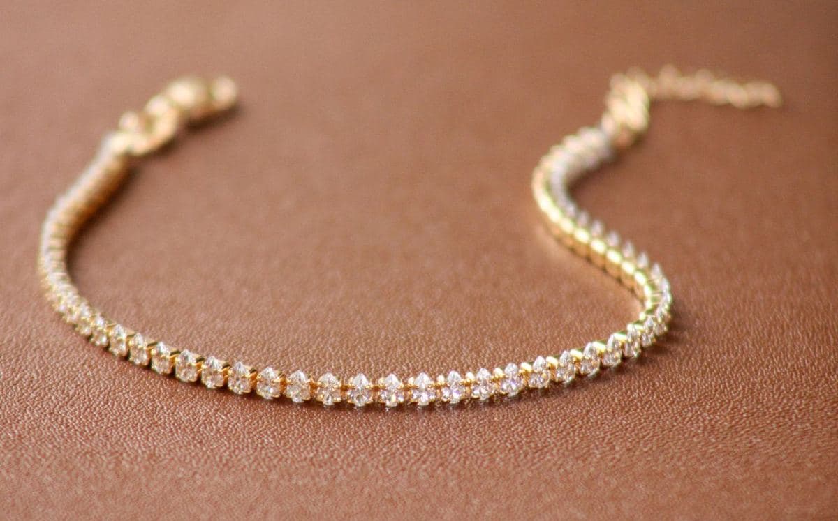 A thin yellow-gold line of small uniform pear-shaped white stones curved in a U on brown leather, with a lobster clasp and extender chain at the ends