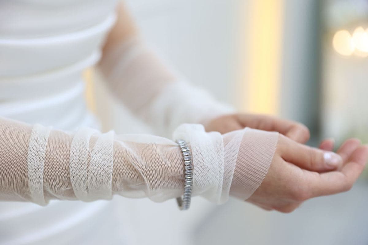 A white-metal bracelet of uniform rectangular step-cut white stones worn over a sheer tulle bridal sleeve, no face shown