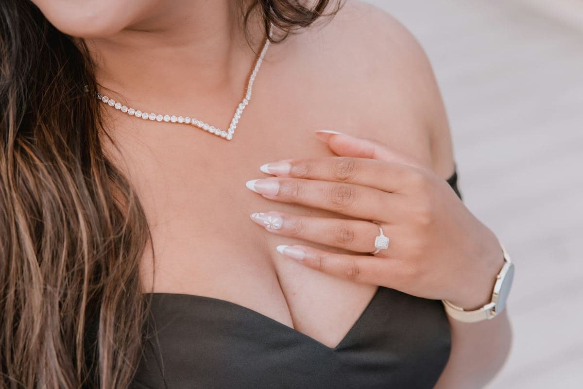 Woman wearing a petite round-stone tennis necklace with a V-shaped center drop, white metal, hand with ring on chest