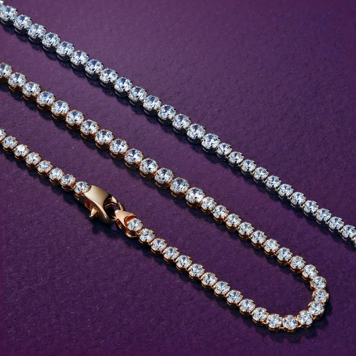 Flat-lay of a four-prong round-stone tennis chain in rose gold with lobster clasp, plus a second white-metal tennis chain running across the top