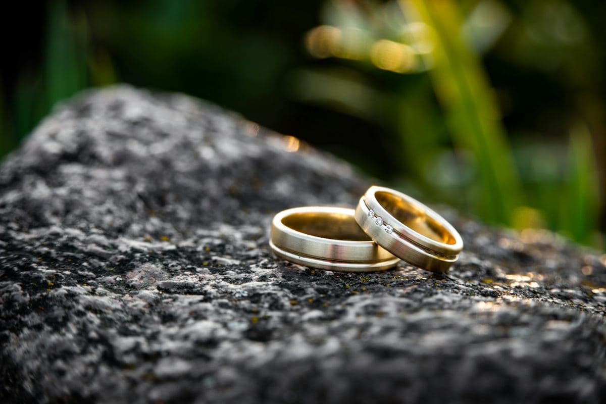 Two brushed yellow gold bands with polished grooved edges, the narrower one set with three small round stones