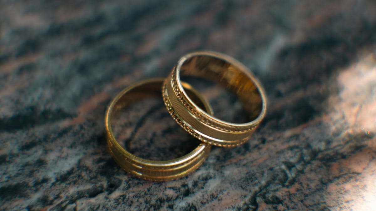 Two yellow gold bands with engraved grooves and milgrain beading, overlapping on granite