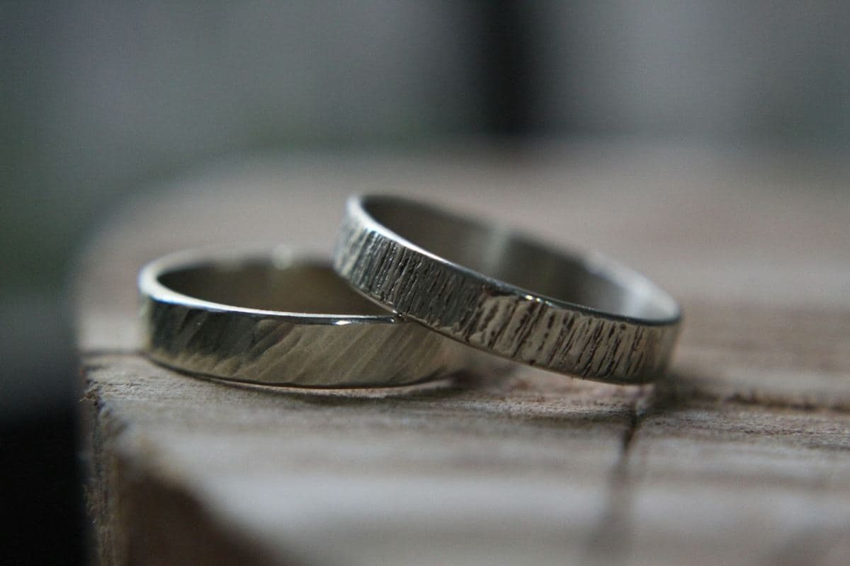 Two flat white-metal bands with hand-textured bark/hammered finishes resting together