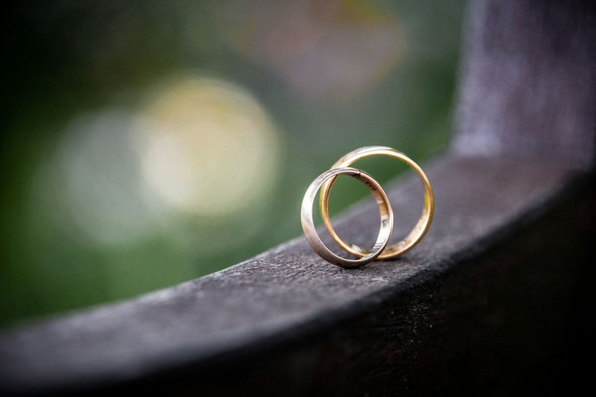 A plain white-metal band standing inside a plain yellow gold band on a dark ledge