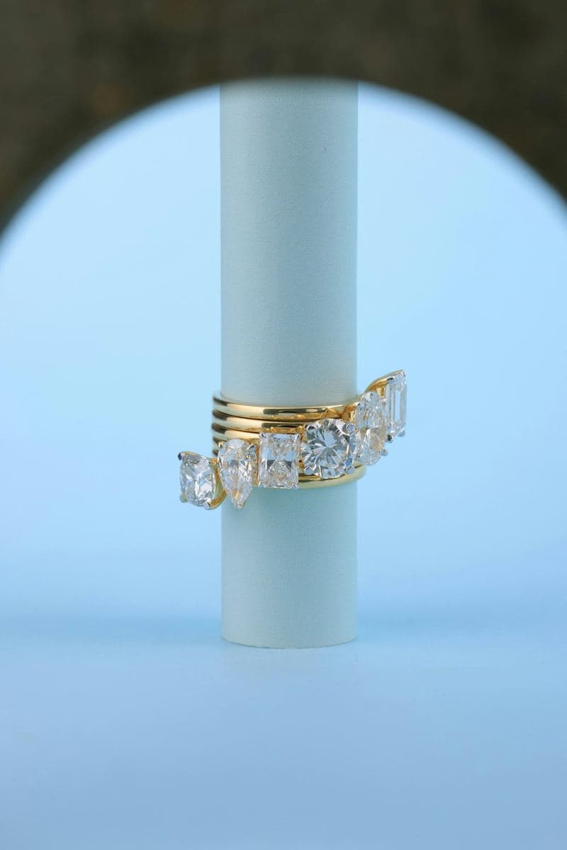 A stack of polished yellow gold bands with large prong-set stones of mixed shapes (cushion, pear, radiant, round, oval, emerald)