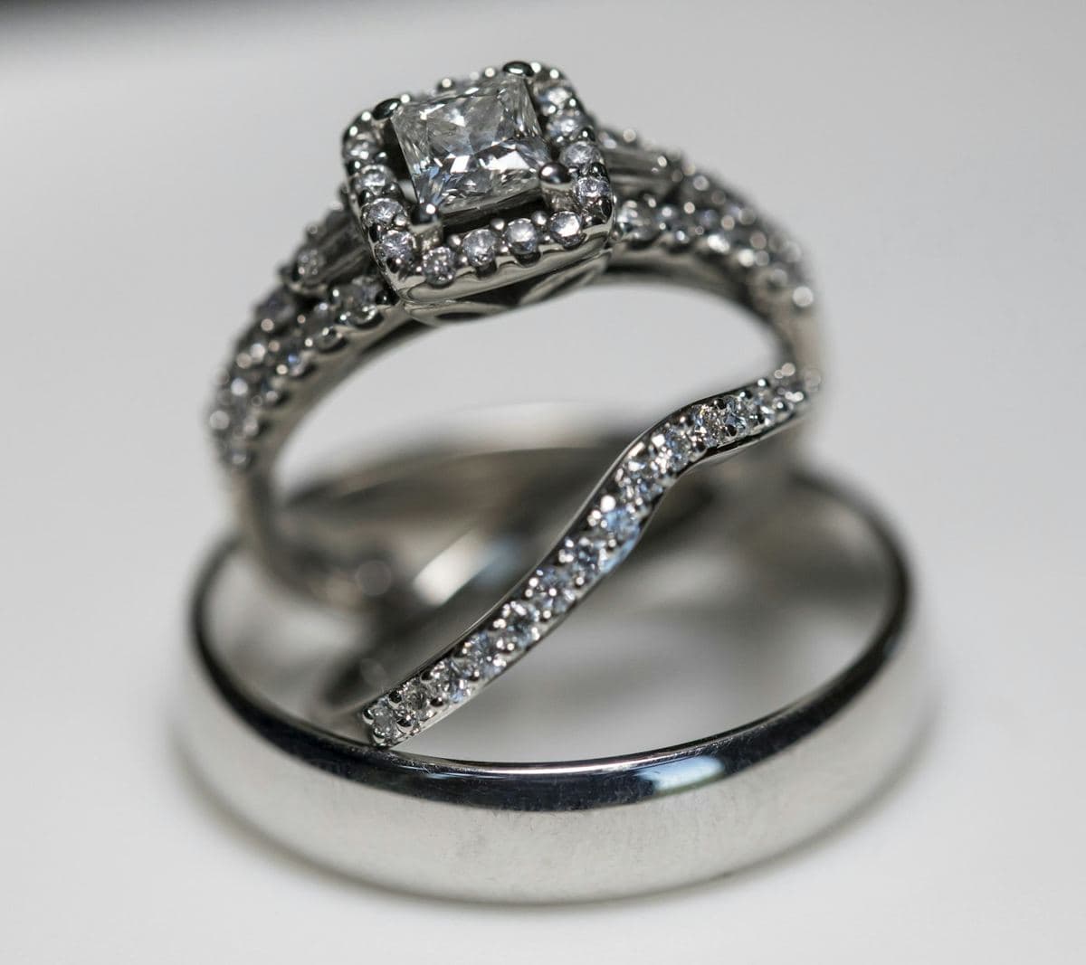 Princess-cut halo engagement ring with a contoured pave band, standing in a plain polished white men's band