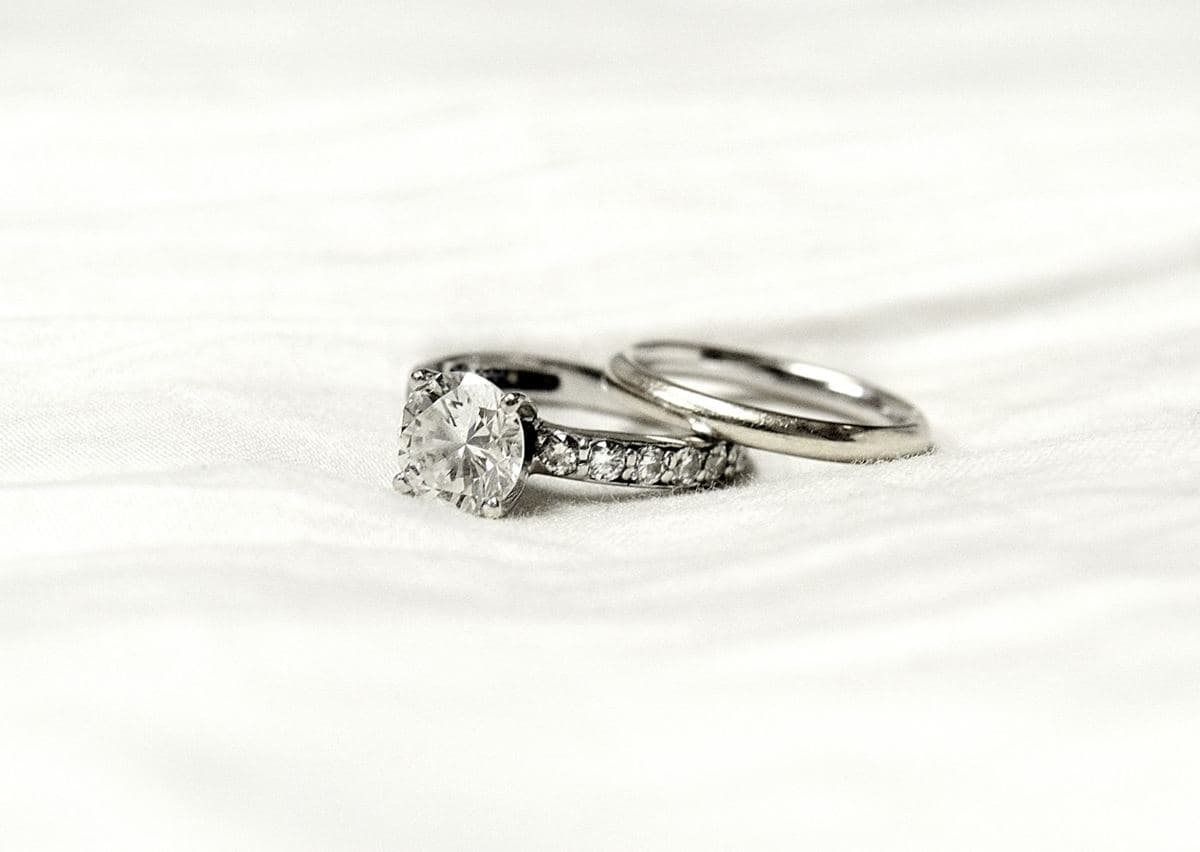 A round four-prong solitaire with a stone shank beside a plain white-metal band