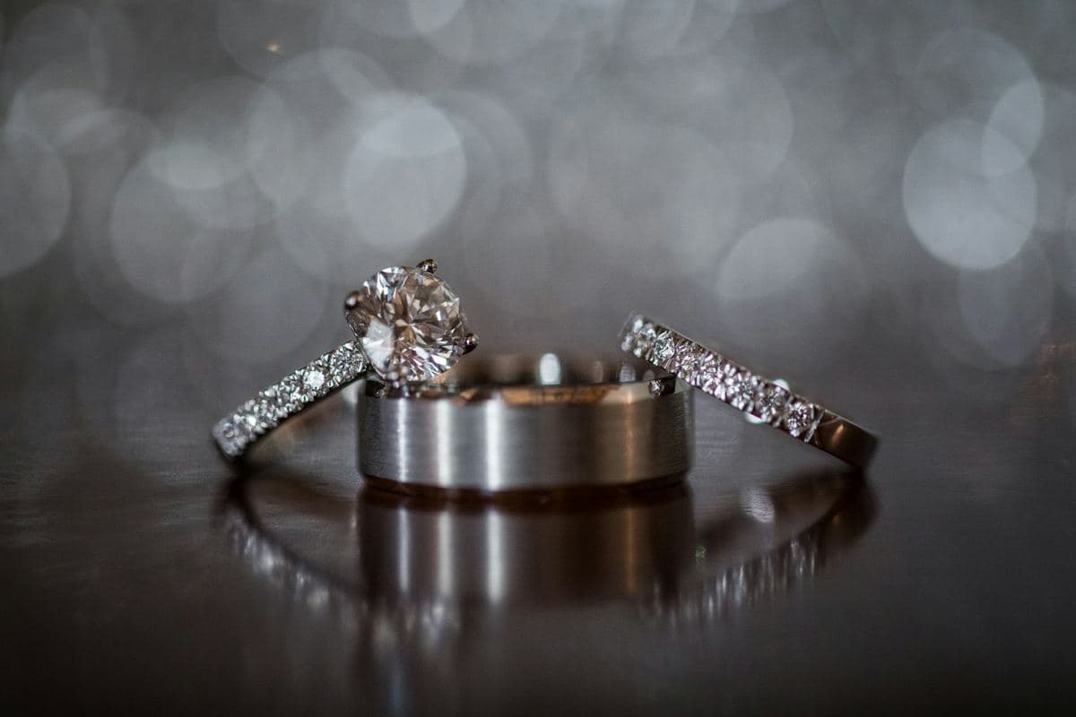 A round solitaire with a stone shank, a brushed white men's band and a stone wedding band, all white metal